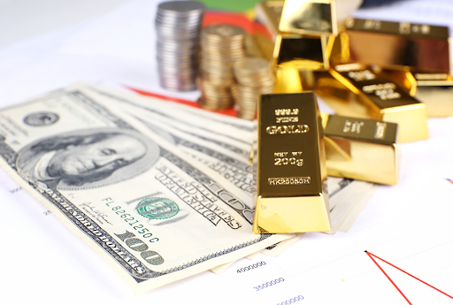 Gold bars, US dollar bills, and coin stacks on financial charts, symbolizing investment strategy and wealth planning.