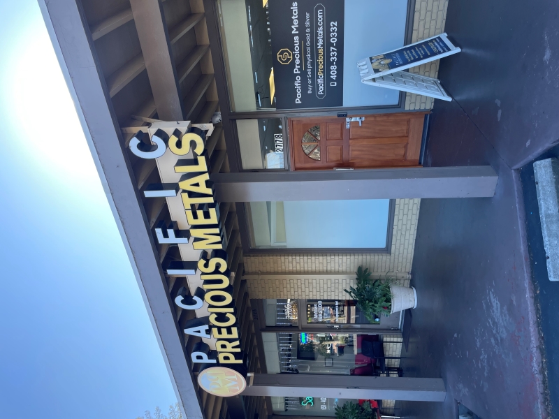 Exterior of Pacific Precious Metals store with signage, contact info, and sidewalk display board in front.