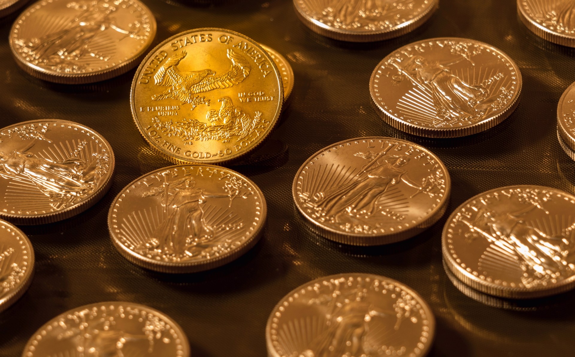 A collection of gold American Eagle coins scattered on a reflective dark surface under warm lighting.