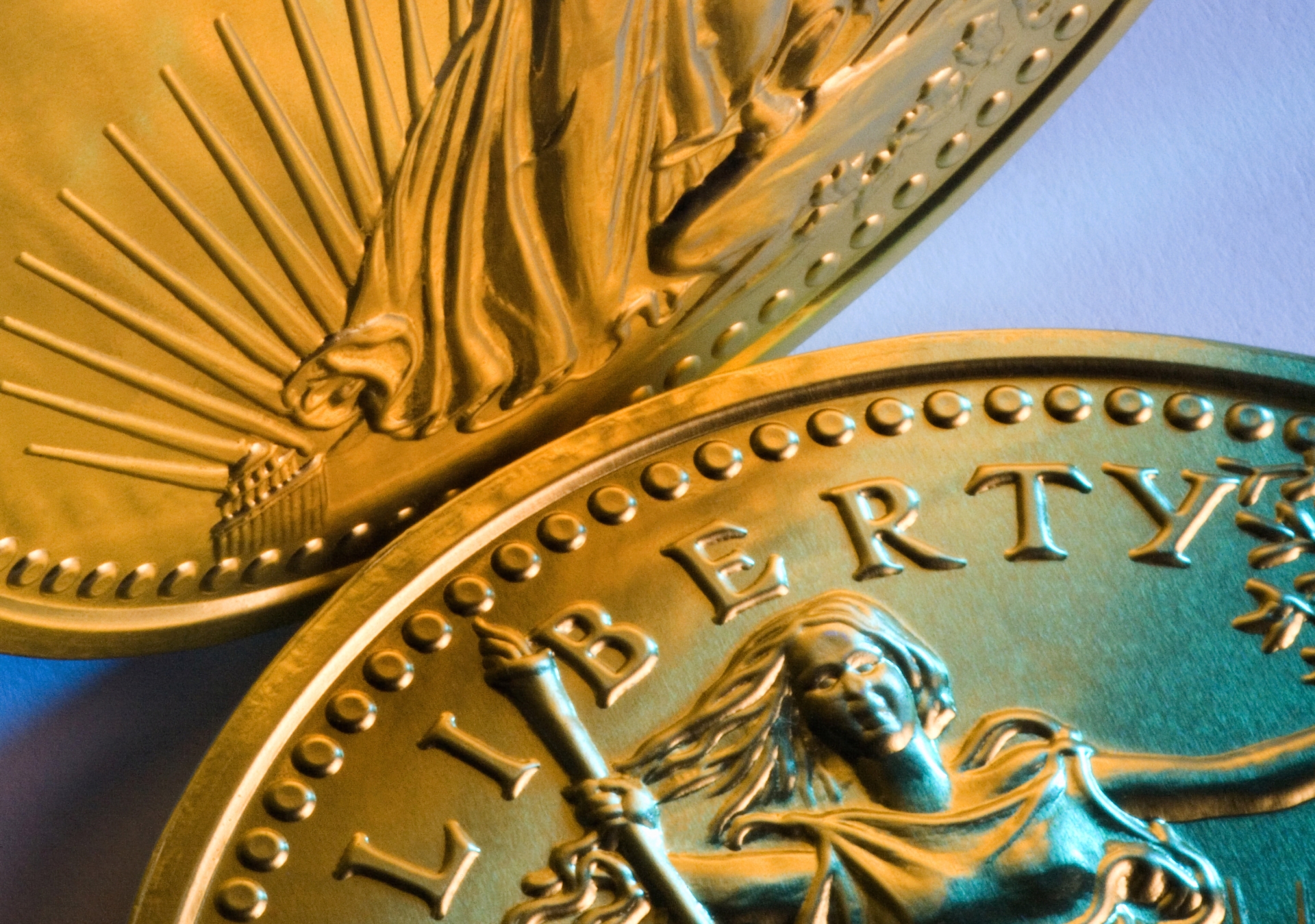 Extreme close-up of a gold American Eagle coin showing the "LIBERTY" text and olive branch.