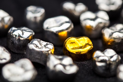 Close-up of shiny silver and gold metal nuggets on a black surface, with one bright gold nugget standing out.