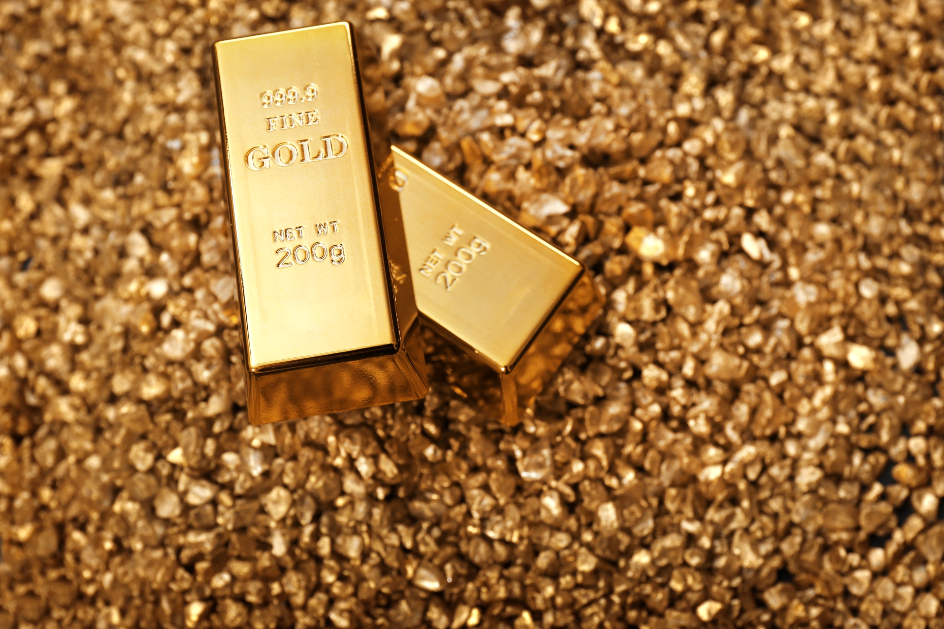 Two 200-gram fine gold bars resting on a large pile of glistening gold nuggets or coarse flakes.