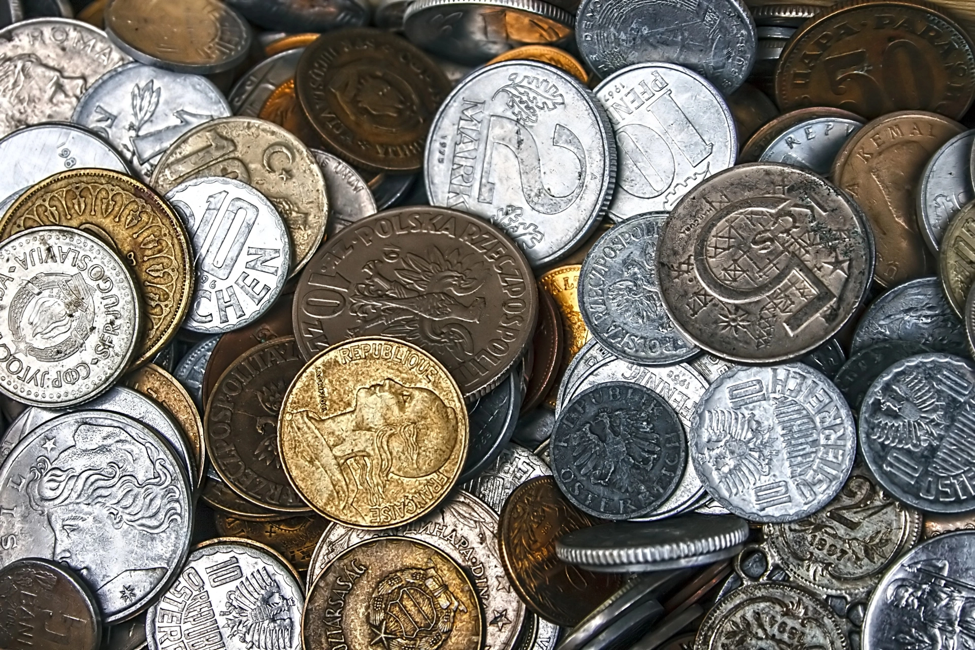 Assorted vintage world coins in silver, bronze, and gold tones displayed in a mixed coin collection.