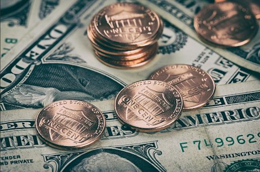 Stacked and scattered U.S. one-cent coins on top of hundred-dollar bills, symbolizing inflation and currency devaluation.