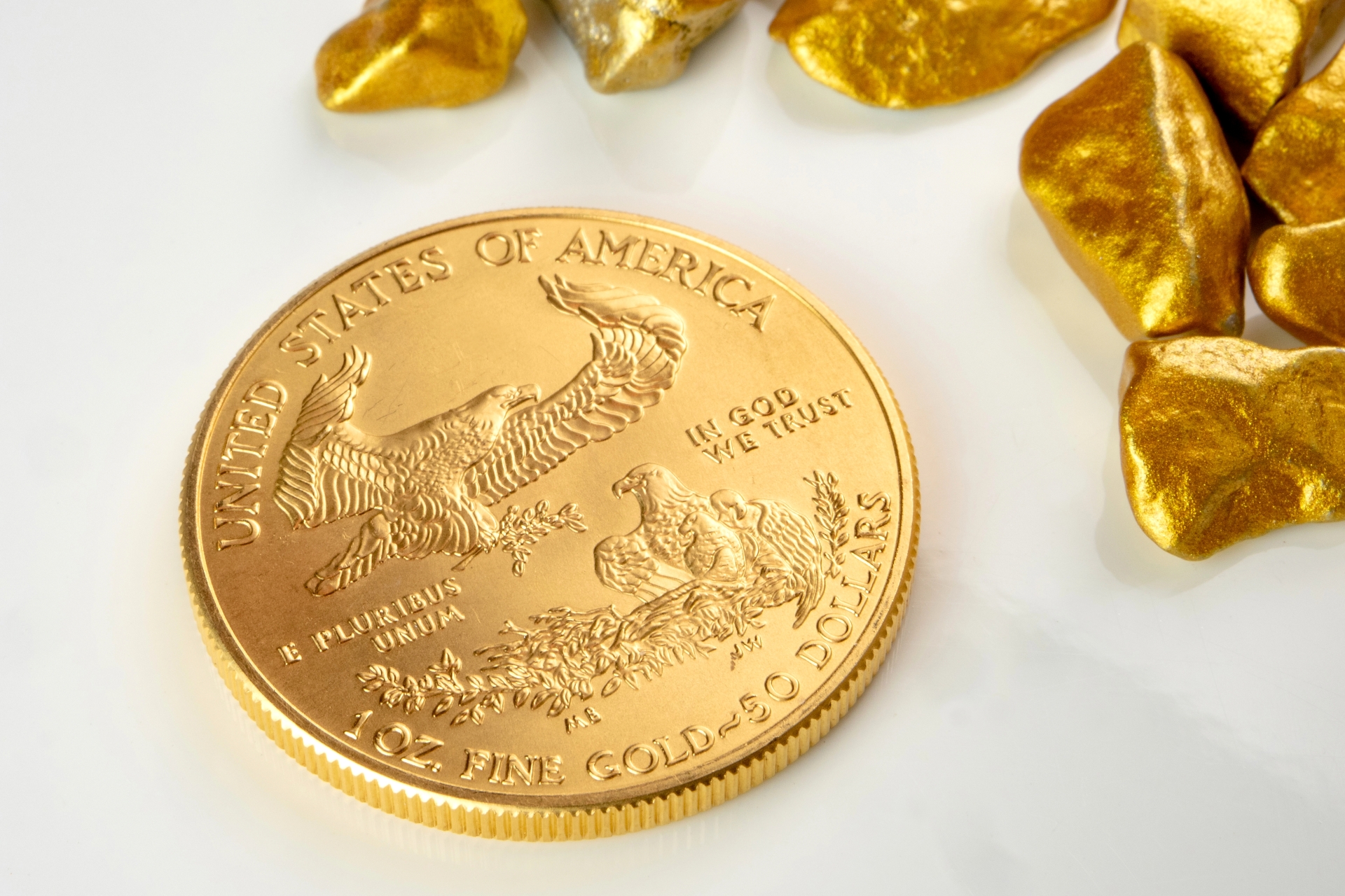 Reverse side of a 1oz gold American Eagle coin featuring a family of eagles, next to several gold nuggets.