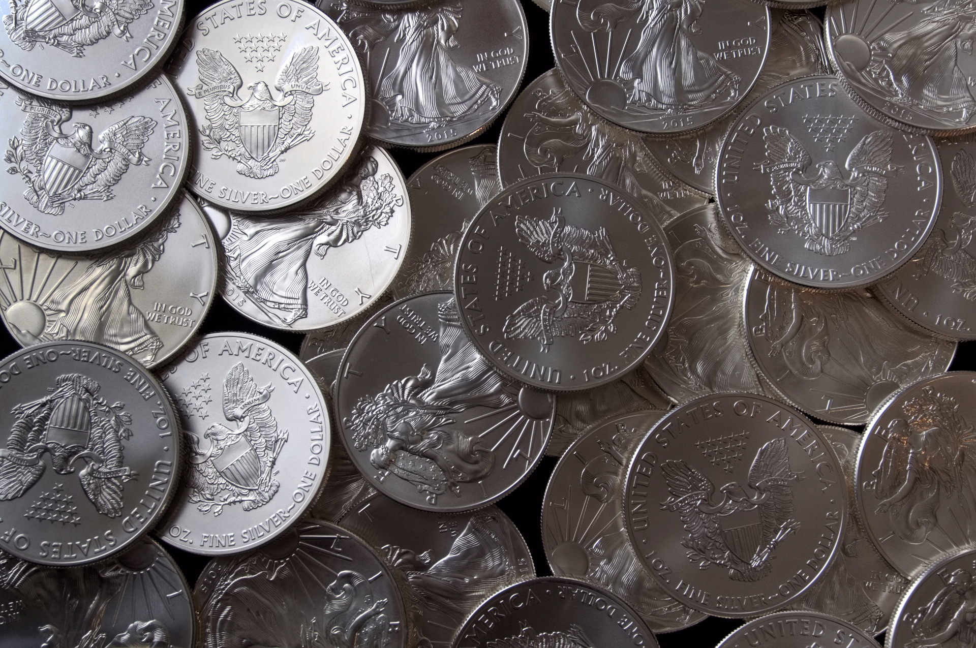 A dense pile of American Silver Eagle one-dollar coins showing both the eagle and Walking Liberty sides.