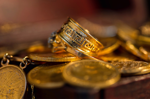 'Intricately designed gold ring resting on a bed of gold coins, representing heirloom jewelry and lasting value.'