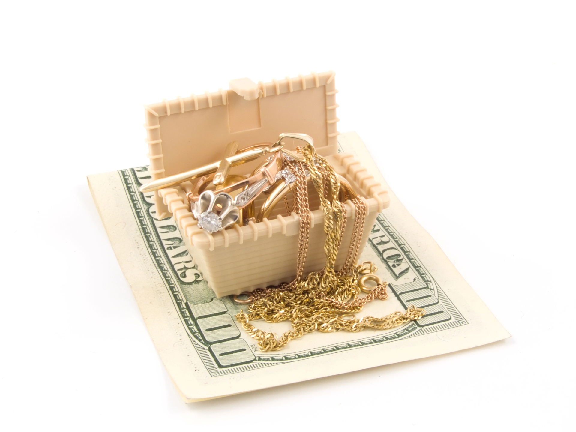  A small tan treasure chest overflowing with gold rings and necklaces sitting on top of a hundred-dollar bill.