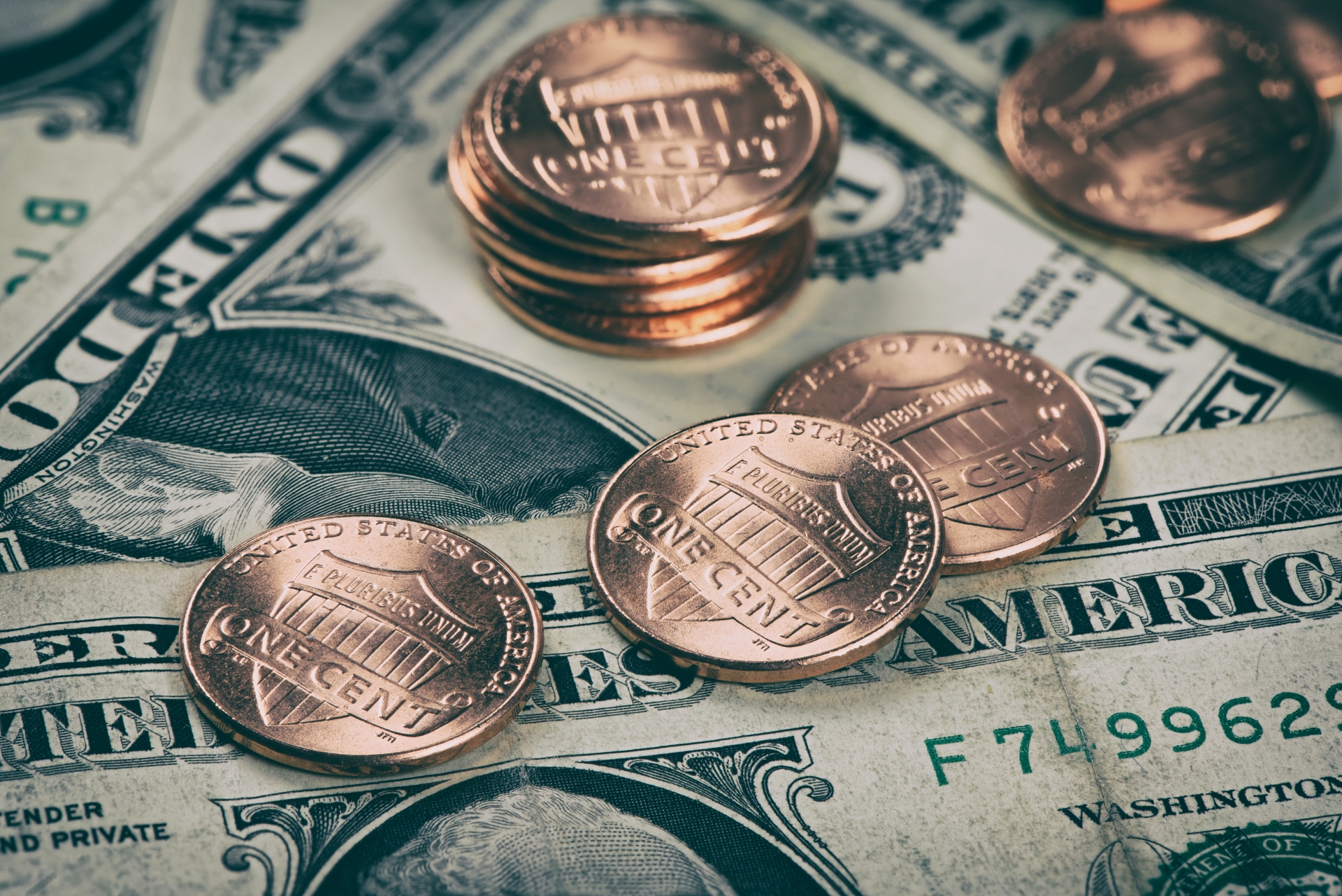 A close-up of several bronze US pennies stacked and spread across a bed of one-dollar bills.