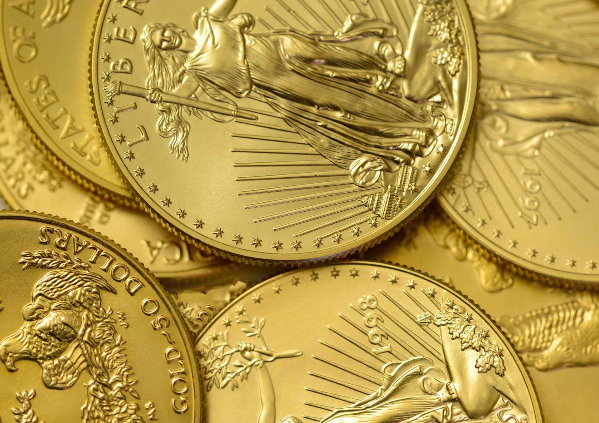 A close-up of multiple US gold American Eagle bullion coins scattered across a surface.