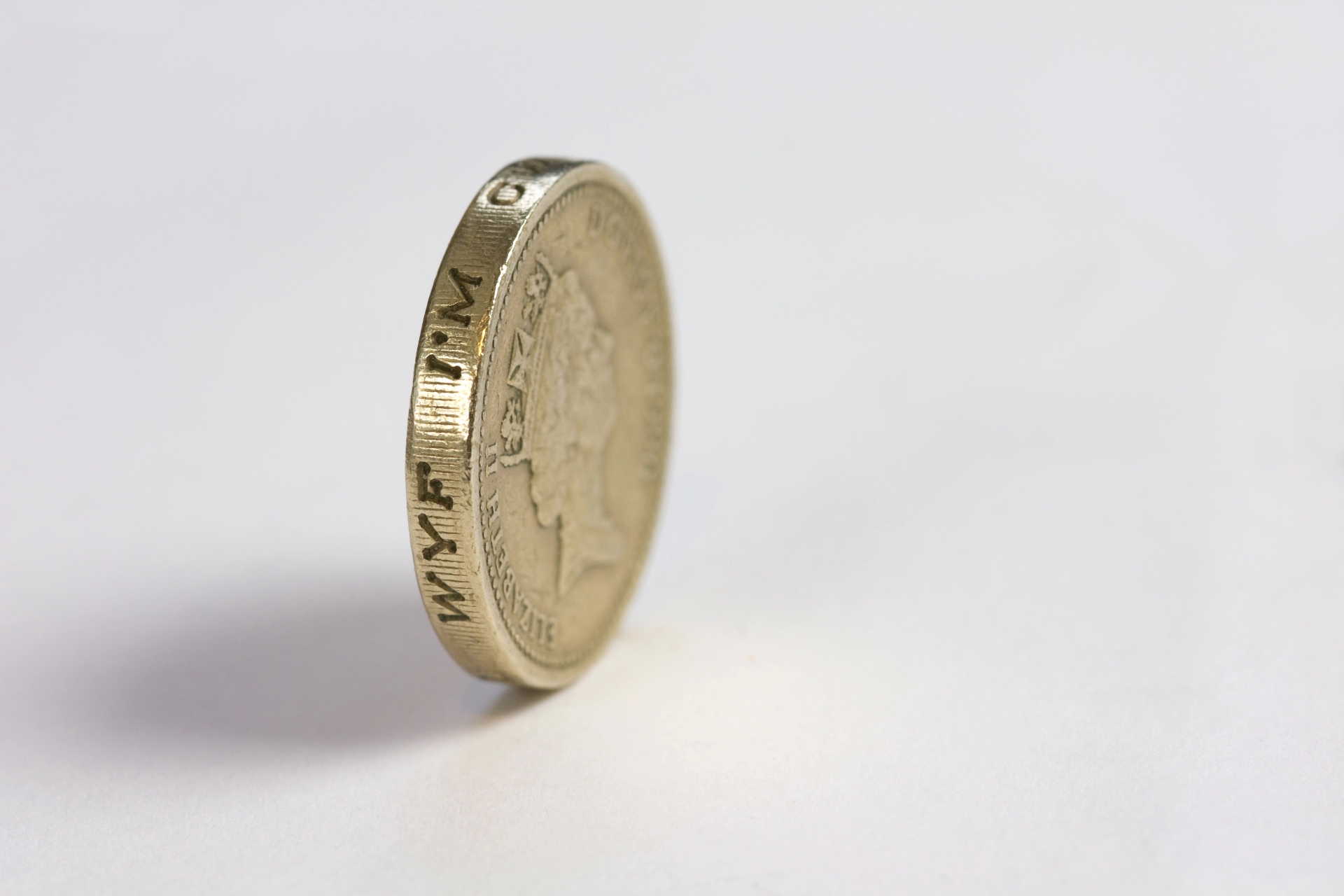 Side view of a single British one-pound coin standing vertically on its edge against a plain white background.