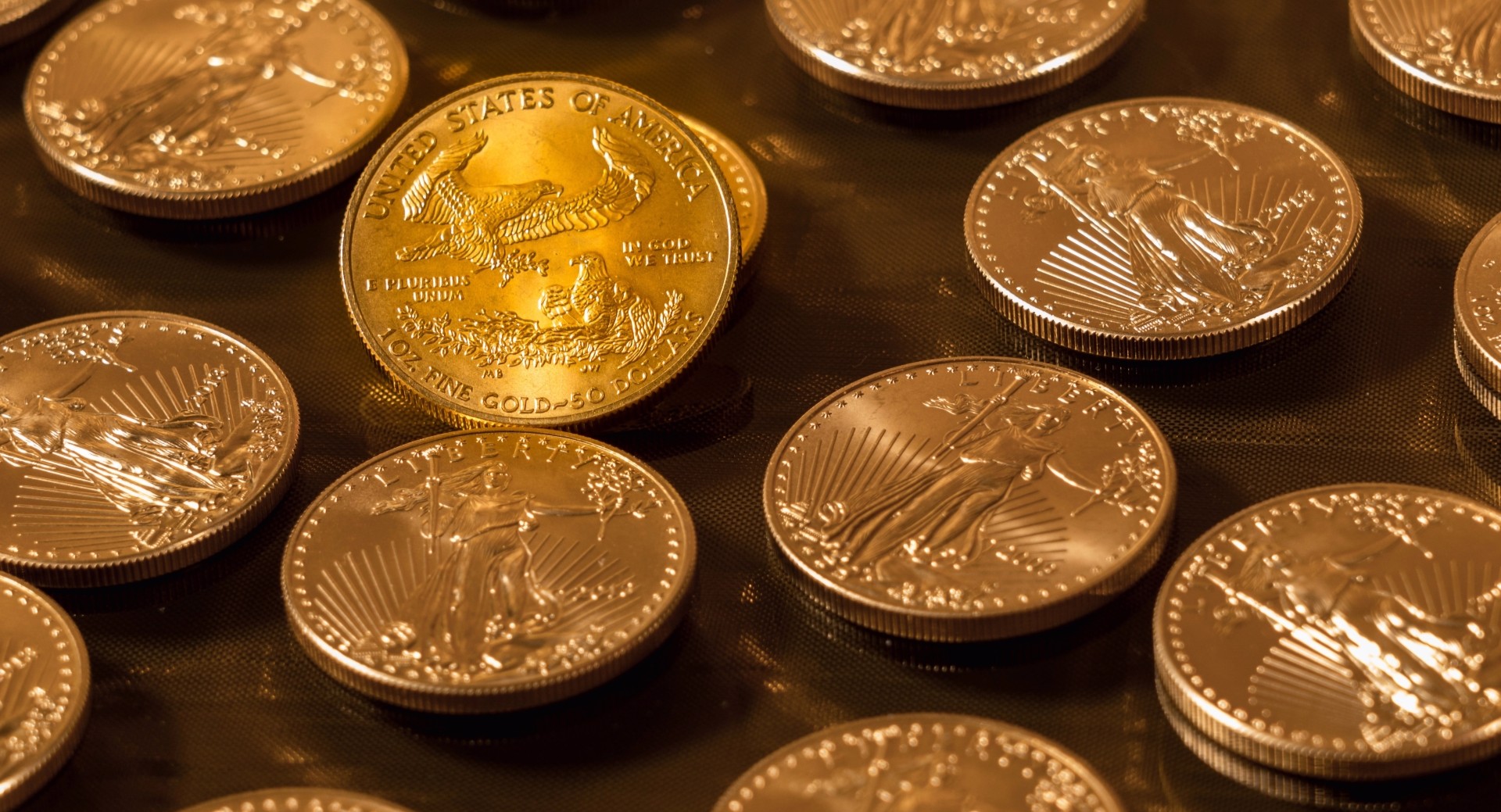 Several gold coins with various designs scattered on a dark, reflective surface.