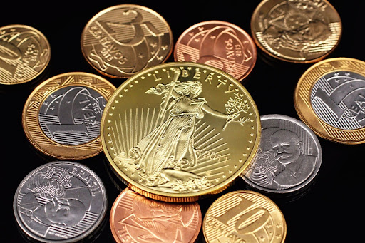 Gold American Eagle coin surrounded by international currency coins including Brazilian real and centavos on black background.