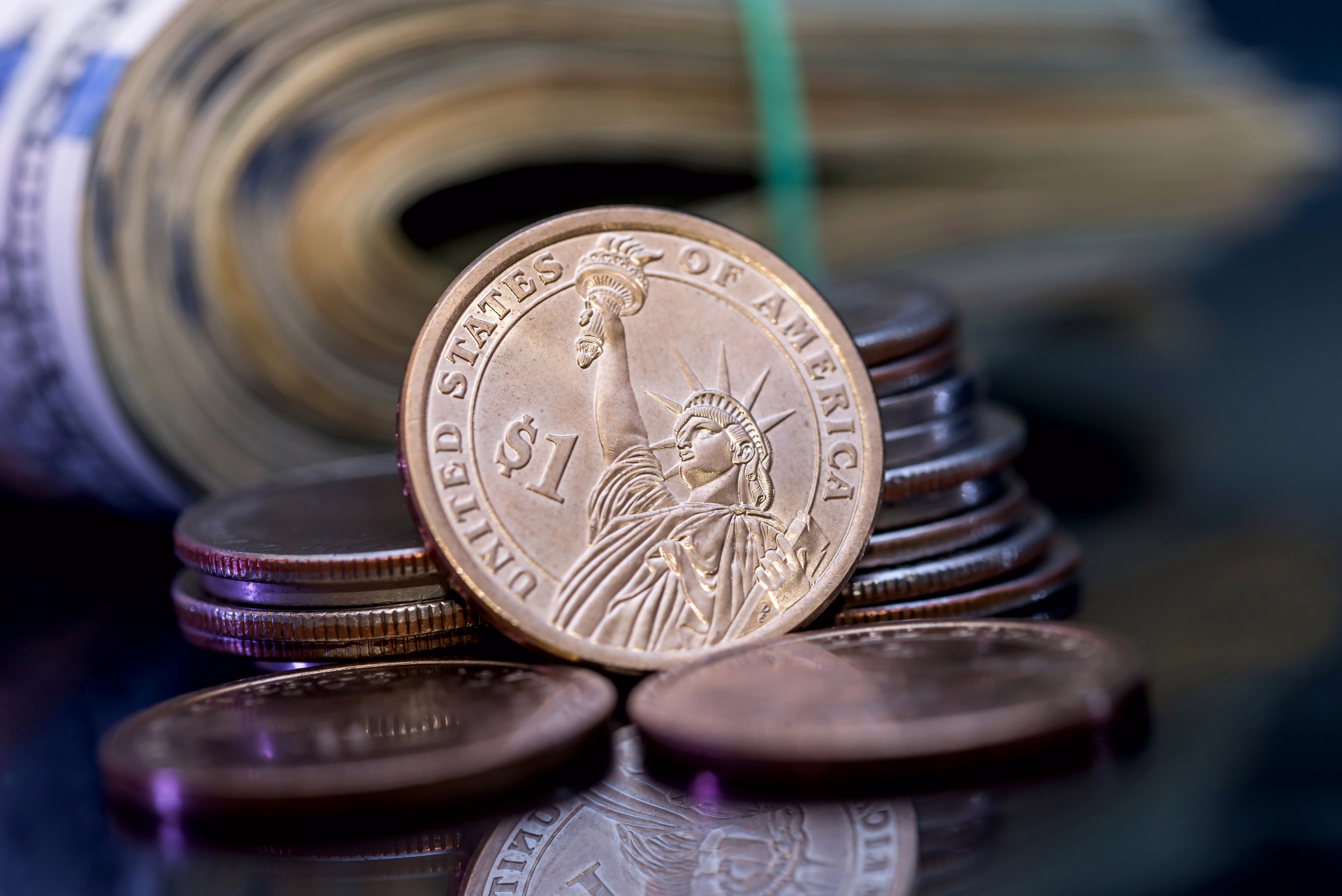 A close-up of a US Presidential $1 coin featuring the Statue of Liberty, positioned in front of a roll of bills. 