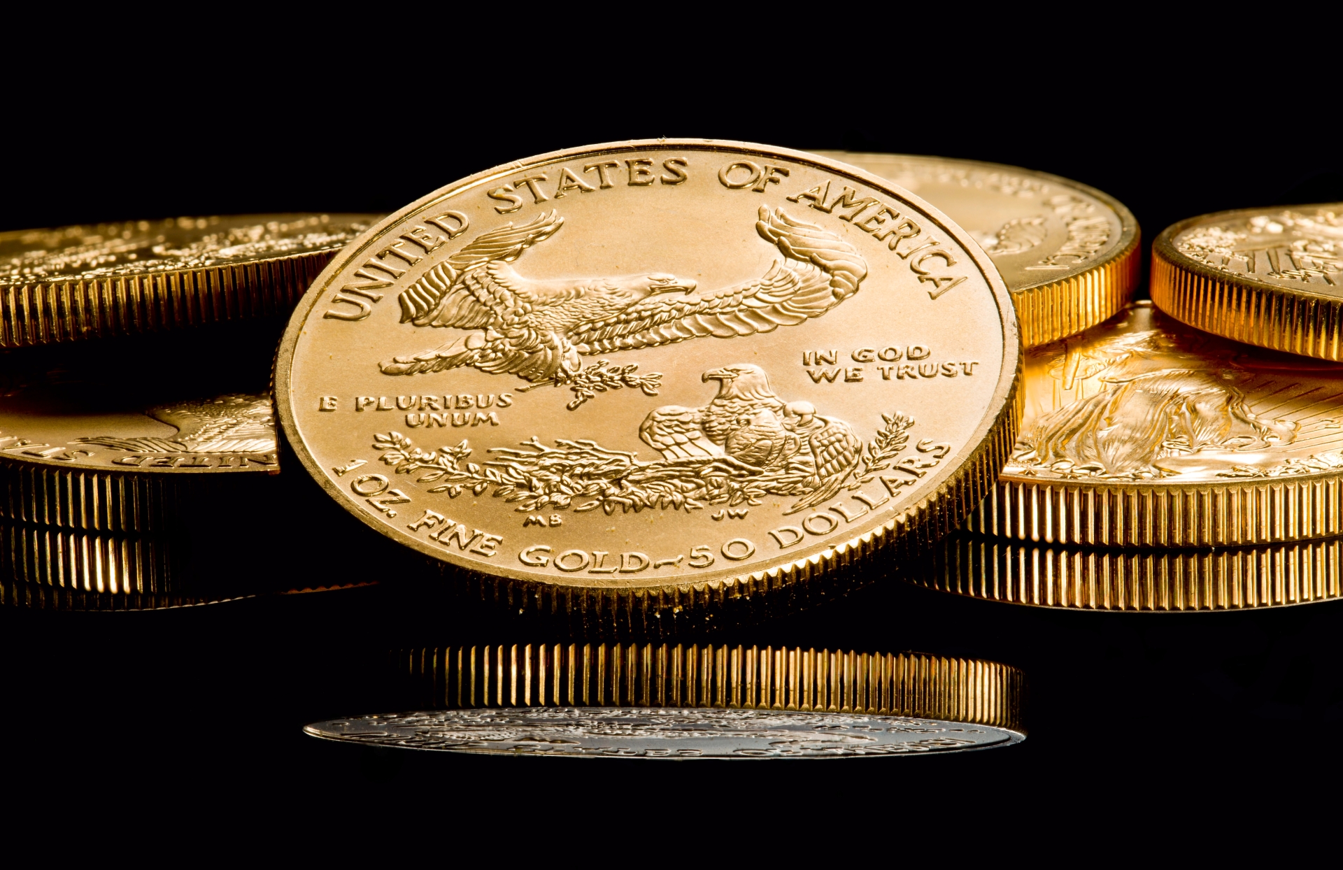 Close-up of several 1oz gold American Eagle $50 coins stacked and displayed against a solid black background.