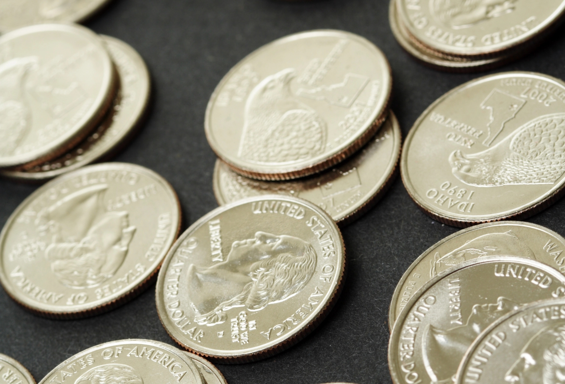 A scattered collection of United States quarter coins on a dark surface, featuring the Idaho state quarter.