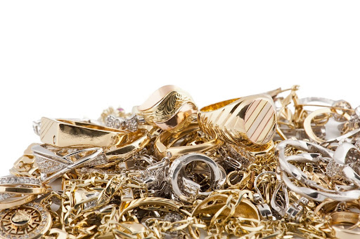 Mixed pile of gold and silver jewelry, including rings and bracelets, stacked chaotically against a white background.