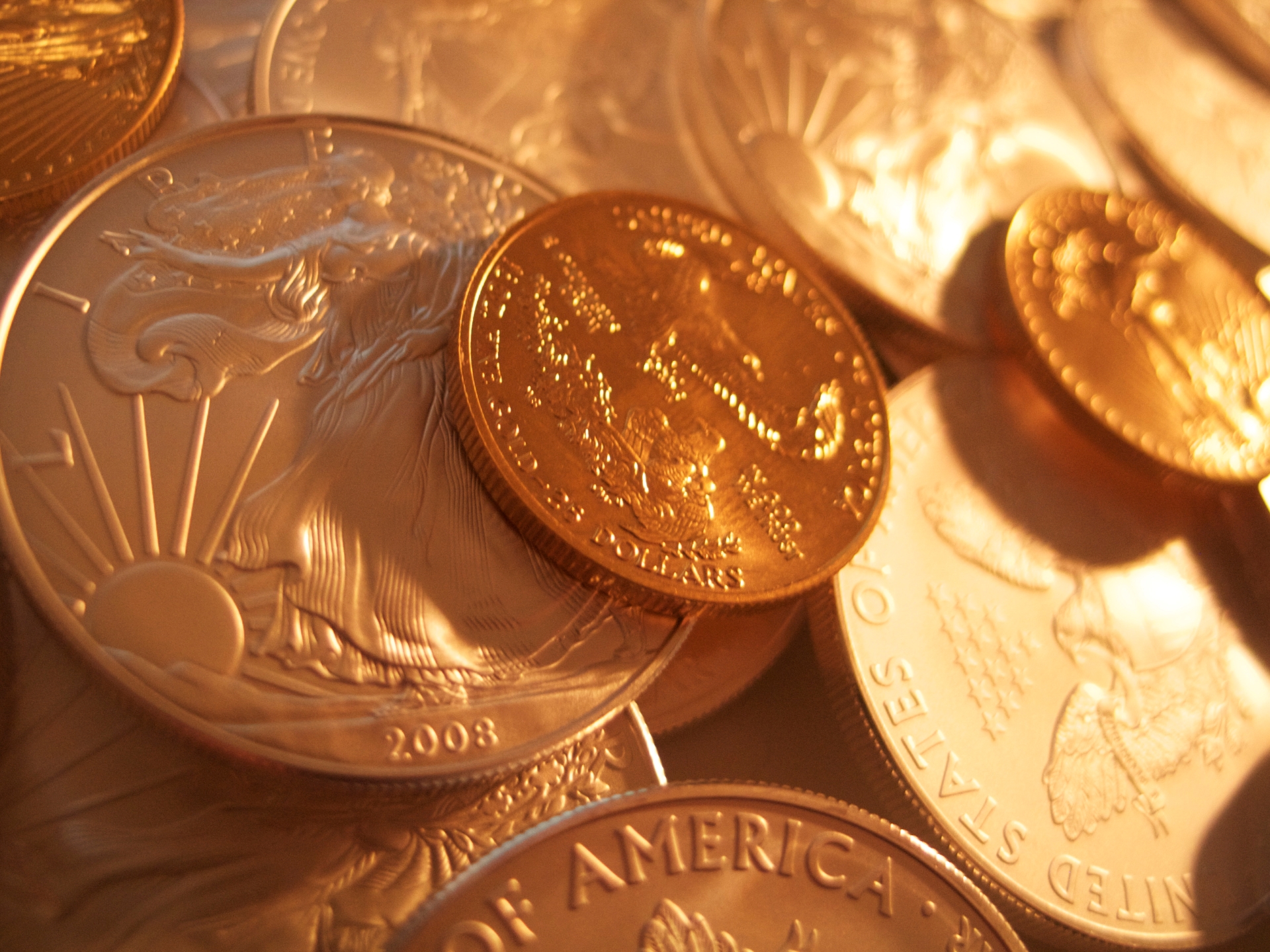  A close-up, warm-toned view of a 2008 American Silver Eagle coin mixed with several gold coins. 
