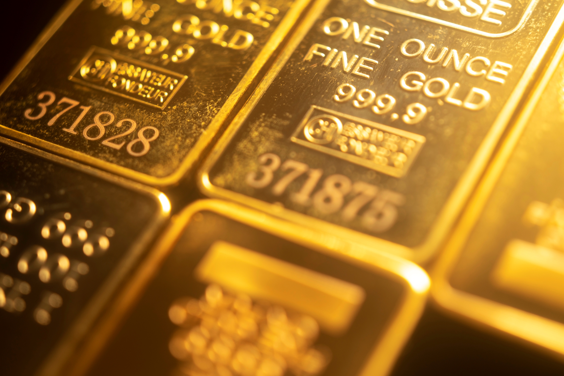 Extreme close-up of several Credit Suisse 1 oz fine gold bullion bars showing official stamps and serial numbers.