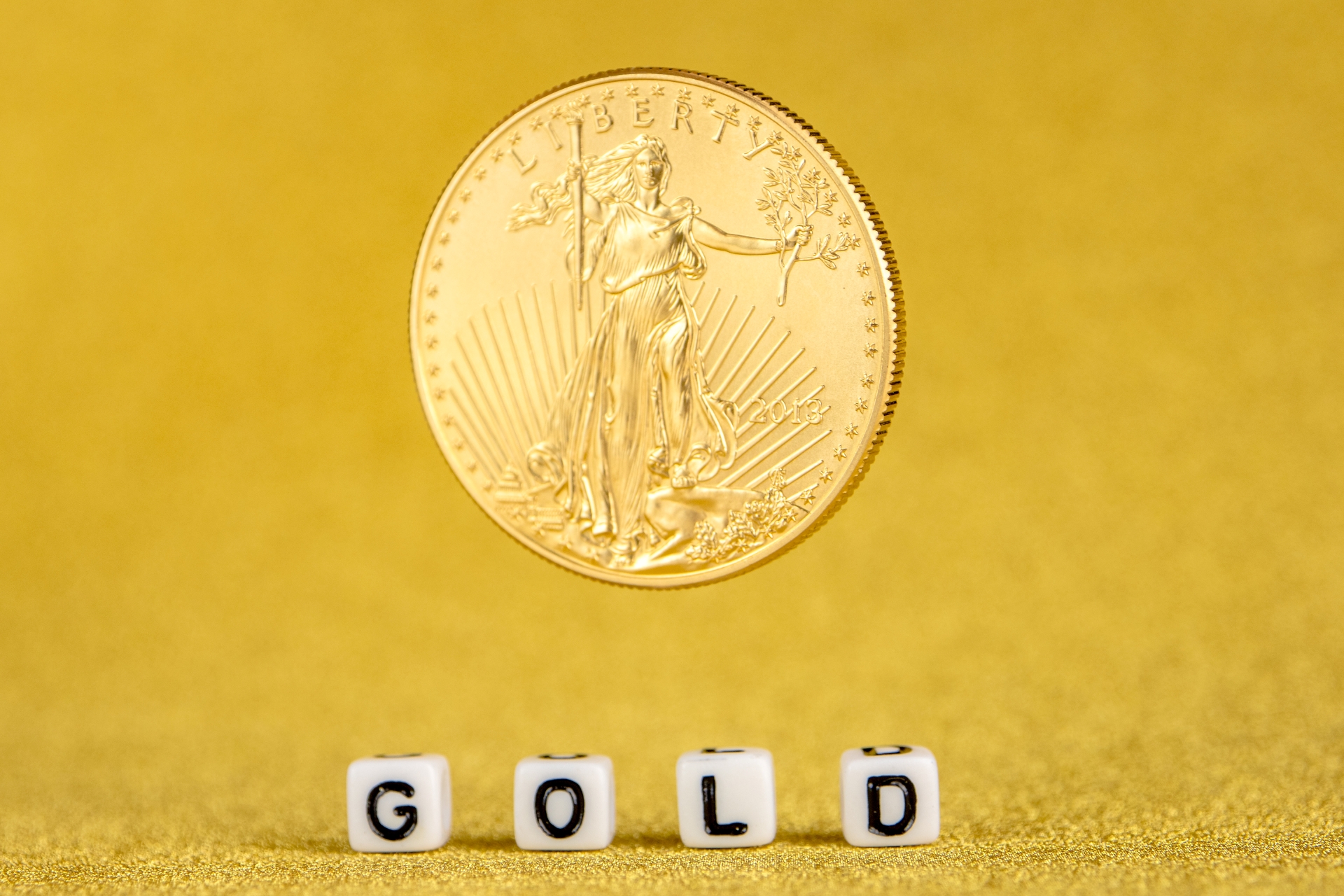 A gold American Eagle coin featuring Lady Liberty standing in mid-air above white cubes that spell out "GOLD."