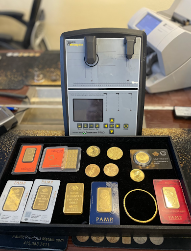 A gold evaluation machine with a set of gold bars, coins, and certificates from PAMP displayed on a counter.