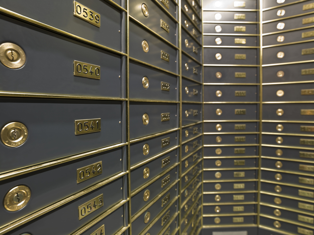 Rows of secure safety deposit boxes with brass keyholes and numbered plaques inside a high-security vault.