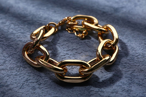 Close-up of a polished gold chain bracelet with large oval links displayed on a textured blue surface.