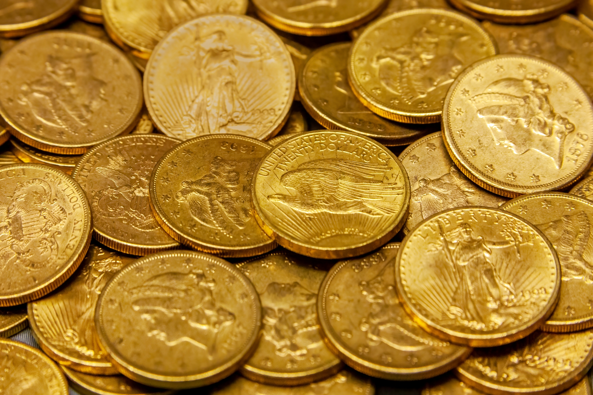A pile of bullion gold coins featuring designs of Lady Liberty, Eagles. 