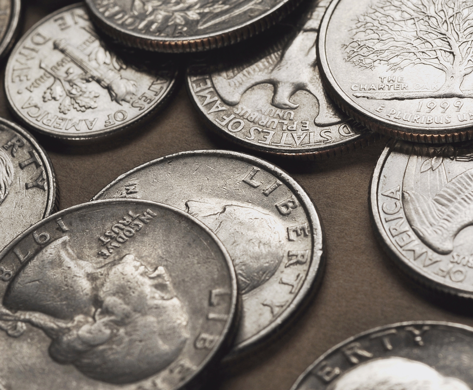 A close-up, scattered pile of various silver United States quarters and a dime showing different mint years.
