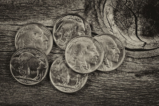 Close-up of vintage Buffalo nickels on rustic wood, symbolizing historical value in physical U.S. coinage.